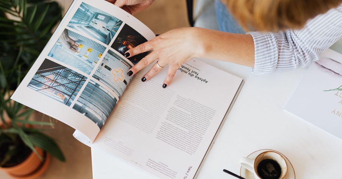 机の上で雑誌をめくる手と、そばに置かれたコーヒーカップ